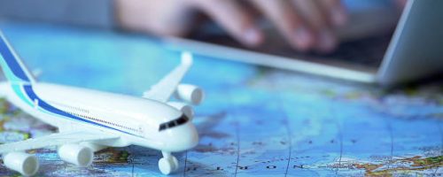 istockphoto-1027397370-612×612 Airplane model closeup, defocused person booking flight tickets online on laptop