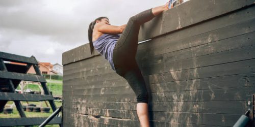 Female participant in an obstacle course climbing a wall