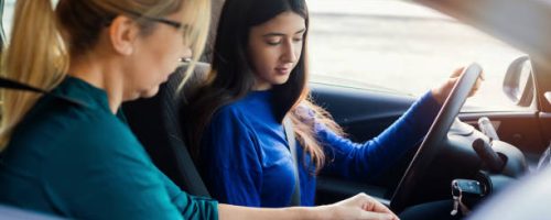istockphoto-1190383810-612×612 A teenage girl sitting behind the steering wheel of a car and listening to her mothers instructions as she drives.